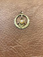 Front view of the gold pendant with cultured pearl on leather surface