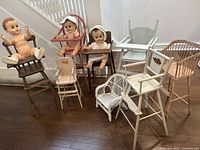 Full set of vintage doll furniture including 8 chairs and 3 dolls arranged on wooden floor in front of stairs.
