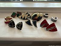 Eight pairs of vintage metal and enamel geometric earrings arranged in two rows on a white surface.