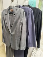 Three women's suit sets in gray, purple, and black hanging on hangers, front view