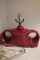 Front view of red ceramic vintage Art Deco style lamp base with electrical socket and attached off-white cord and plug.