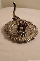 Side view of silver-toned elephant ring holder on ornate decorative plate showing raised trunk and embossed edges