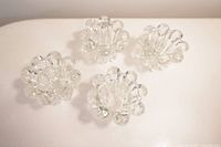 Four clear glass candle holders arranged on a white surface showing the rounded bubble or petal style edge design.