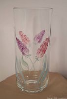 Front view of cylindrical clear glass vase with pink and purple hand-painted flowers and green leaves.