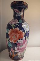Front view of large tall ceramic vase with large pink, red, white flowers and green leaves on dark blue background, detailed bird near neck.