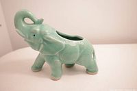 Front side view of the mint green ceramic elephant planter displaying the full body with trunk raised and visible planter opening on the back.