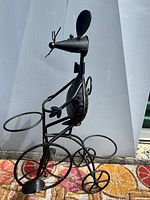 Metal mouse planter holder missing one ear, standing on a colorful carpet against a white backdrop.