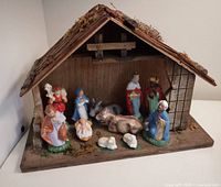 Full view of vintage nativity scene including stable and all figurines arranged inside and around the stable on a wooden base