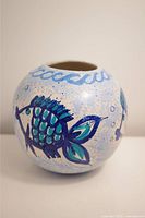 Front view of round pottery vase with painted blue and green fish and wave patterns on a light background.