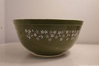 Side view of the green Pyrex mixing bowl with white floral pattern showing scratches.