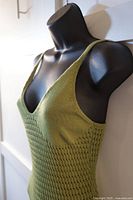 Side-angle view of green knit dress on black mannequin, showing V-neckline and knit texture.