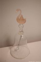 Glass bell with clear bell base and peach-colored swan handle, viewed from two angles showing chain clapper inside.