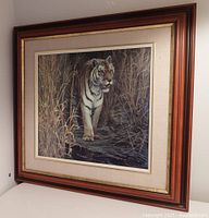 Framed tiger print showing full wooden frame, glass covering, and beige fabric mat with gold trim inner border.