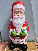 Front view of vintage blow mold Santa, showing facial details, red suit, and black boots.