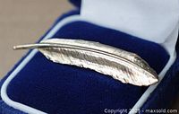 Silver-tone vintage feather brooch laid inside a blue and white jewelry box showing textured feather details.