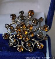 Front view of vintage round metal brooch with amber colored rhinestones set in swirl floral design.