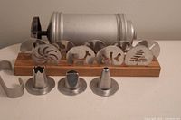 Front view of vintage metal icing set showing dispenser, wooden stand, metal stencil discs and nozzle tips