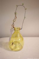 Yellow translucent glass wasp bug catcher with wire hanger decorated with green beads, shown from front angle.