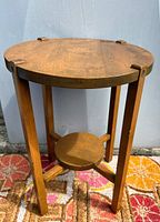 Full view of round vintage wooden table with a smaller round shelf below and four legs, placed on a colorful floor mat against a white wall.