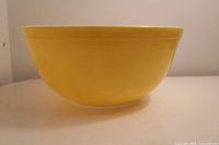 Side view of the larger yellow Pyrex mixing bowl showing solid yellow exterior and white interior with some visible surface scratches.