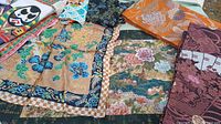 Top view of assorted silk fabrics including tan floral, navy scenic, orange brocade, purple patterned and others
