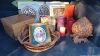 Full lot overview showing framed panels, tin box, basket with framed print, candles, pinecone sculpture, floral box