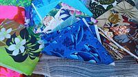 Assortment of folded fabrics showing multiple patterns including orca, tropical leaves, flowers and stripes