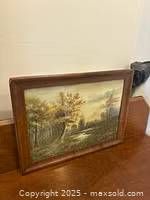 Photo of antique rustic landscape oil painting in wooden frame leaning on a table against a wall.