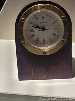 Front view of compact rectangular desk clock with mahogany finish and brass bezel surrounding white dial with Roman numerals.