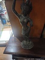 Front view of brass goddess statue on wooden table.