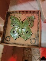 Square pottery plate with a raised green butterfly on beige background with patterned border