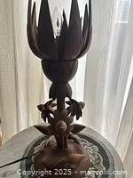 Photo of a carved sandalwood lamp with a lotus motif. The lamp has a detailed base with floral carvings, three smaller lotus buds positioned on the stem, and one large open lotus flower on top.