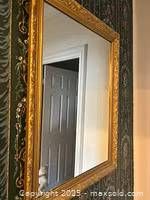 Photo of a rectangular goldleaf wooden carved mirror hanging on a wall, showing carved floral and scroll details and clear glass reflection.
