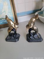 Pair of solid brass heavy seal bookends on a countertop with a painting and wash basin in the background.