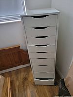 Photo of white IKEA Alex 9 drawer storage cabinet, tall and narrow with nine drawers; one drawer is partially open showing functionality.