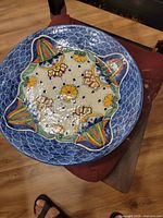Top-down view of large round hand-painted Mexican ceramic plate featuring blue patterned rim and central orange, yellow, and green decorative motifs.