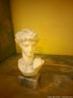 Blurry image showing a small marble bust sculpture resembling David, on a wooden surface with a yellow background.