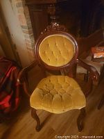 Front view of mustard yellow upholstered wooden accent chair with carved details and tufted button design on backrest and seat.