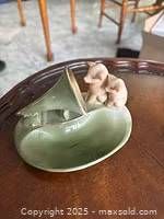 Photo of a green ceramic gramophone shaped trinket holder with two pink piglets on top, sitting on a brown wooden surface.