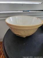 Side view of a ceramic mixing bowl showing embossed decorative exterior and white glazed interior with some discoloration.