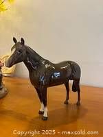 Glossy black porcelain horse figurine with white feet shown from side angle on wooden surface, natural lighting.