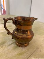 Photo of a solid copper antique water jug with decorative handle showing patina and craftsmanship details.