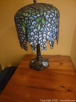Front view of lamp showing stained glass shade with blue and green flower pattern and ornate metal base