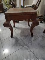 Photo of a solid wood table or footstool showing its rectangular top, carved legs, and decorative scrollwork on supports