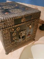 Close-up of antique treasure chest showing ornate metal decorations and front handle detail.