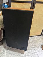 Front view of one speaker showing black cloth grille with HPM-100 badge and wood veneer top edge