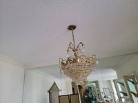 Crystal chandelier hanging from ceiling in room. Large size with multiple tiers of crystal beads and pendants, brass or gold-tone frame and chain.