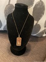 Pendant and chain displayed on black bust against patterned fabric background