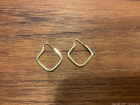 Pair of 10K gold square hoop earrings laid flat on a wooden surface, showing front view.