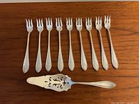 Ten fish forks lined up above a pierced server on a wooden surface